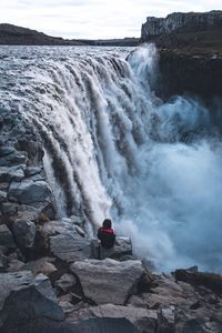 High angle view of woman sitting on rock by waterfall