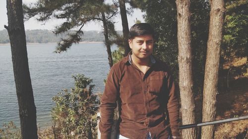 Portrait of man standing by trees against lake