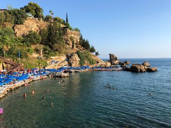 People on rocks by sea against clear blue sky