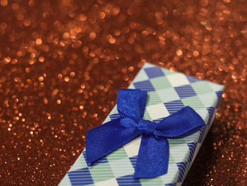 Close-up of christmas gift with blue ribbon on red glittering table