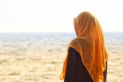 Side view of teenage girl wearing hijab standing at beach against clear sky