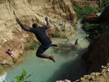 Man jumping off rock at shore