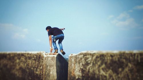 Man jumping over retaining wall against sky