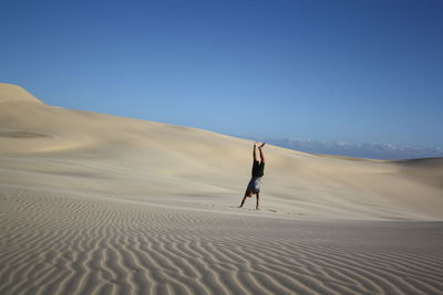 Man performing hand standing in dessert against sky