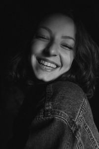 Close-up of happy young woman against black background