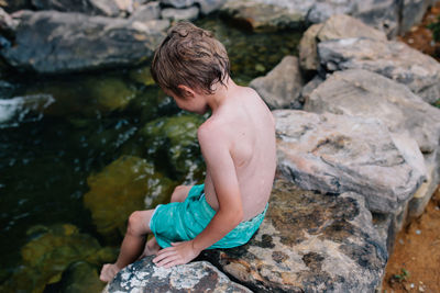 Rear view of shirtless boy on rock
