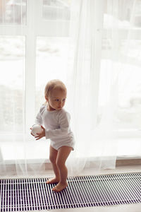 Girl child stands at the window in white clothes at home in winter