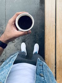 Low section of man holding coffee standing on foot path