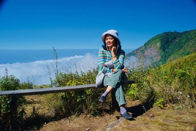 Senior woman sitting on bench at mountain against sky