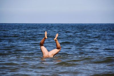 Low section of man swimming in sea against sky