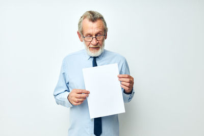 Portrait of man holding paper while standing against white background