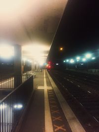 Illuminated railroad station platform against sky at night