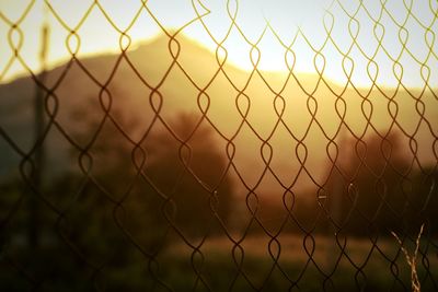 Close-up of chainlink fence against sky during sunset