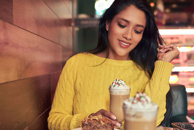 Smiling young woman holding drink in glass at cafe