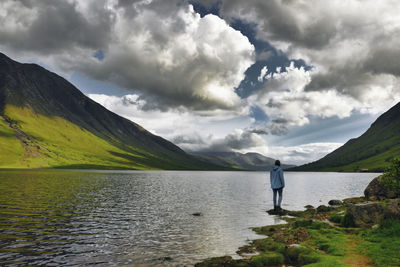 Rear view of woman standing by lake against sky