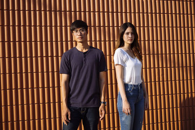 Portrait of young couple standing against brick wall