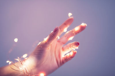 Close-up of hand on illuminated light against sky