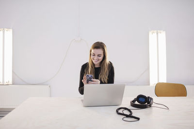 Happy female blogger using smart phone at desk in office