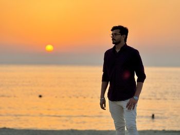 Rear view of man standing at beach during sunset