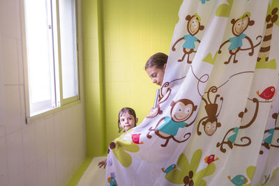 Siblings by curtain in bathtub