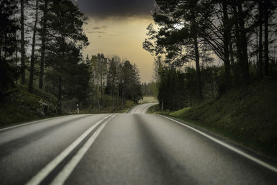 Country road amidst trees in forest against sky