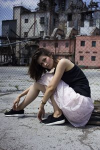 Portrait of young woman sitting on building in city