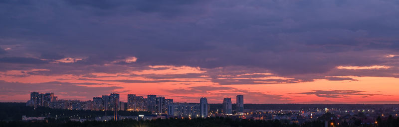 Illuminated buildings in city against sky during sunset