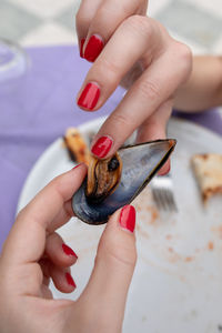 Woman with red nail polish holding mussel over plate at table