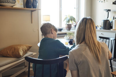 Rear view of mother helping son with homework at home