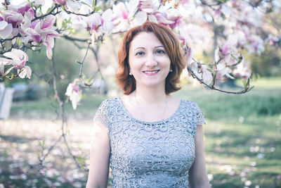 Cheerful middle aged armenian woman in elegant dress under magnolia blooming tree. spring portrait 