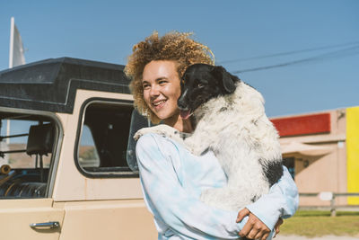 Smiling young blond woman carrying dog while looking away on sunny day