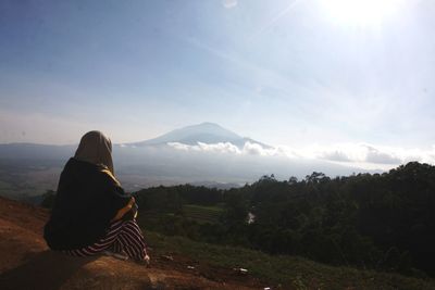 Rear view of woman sitting on mountain against sky