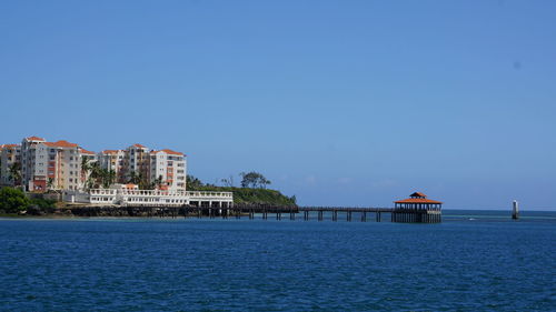 Scenic view of sea by buildings against clear blue sky