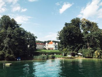 Trees by lake against buildings in city