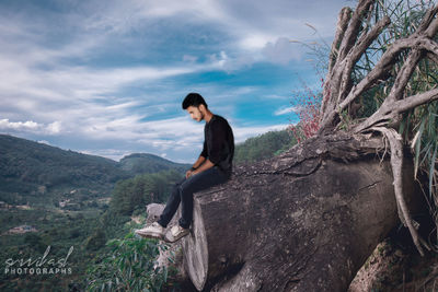 Side view of man sitting on rock against sky