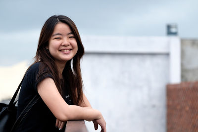 Portrait of smiling young woman standing against sky