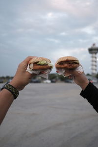 Cropped hands of couple holding burger outdoors