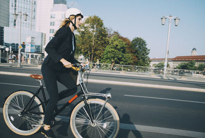 Side view of businesswoman riding bicycle on city street against sky