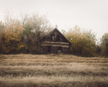 Abandoned house on field by trees against sky