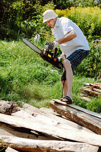 A man in shorts and a panama saws a tree with a chainsaw in his hands