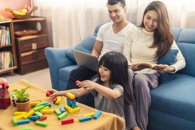 Smiling girl playing with toy blocks by parents in living room at home