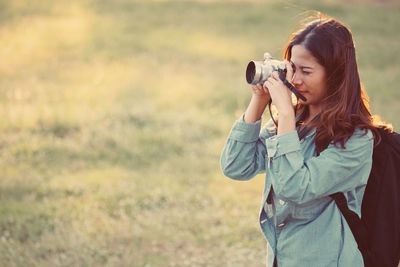 Young woman photographing while standing on grassy field
