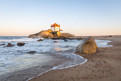 Lighthouse on beach by sea against sky during sunset