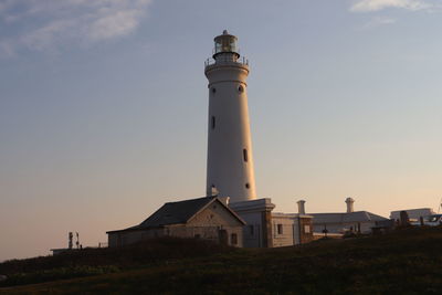 Low angle view of lighthouse by building against sky during sunset