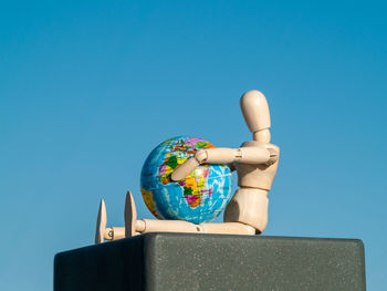 Low angle view of wooden figurine with globe against clear blue sky