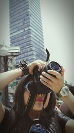 Close-up portrait of young woman holding camera in city