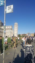 People walking on street in city against clear blue sky