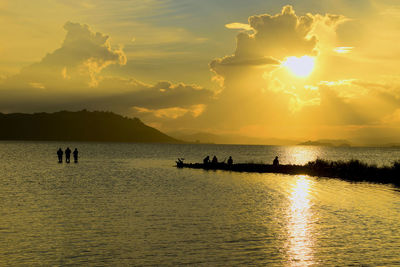 Silhouette people in sea against sky during sunset