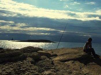 Fishing rod on rock by sea against sky