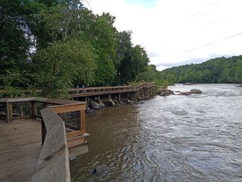 Footbridge over river in forest against sky